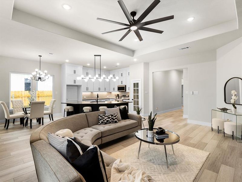 Living room with a chandelier, light wood-type flooring, a ceiling fan, recessed lighting, and a tray ceiling