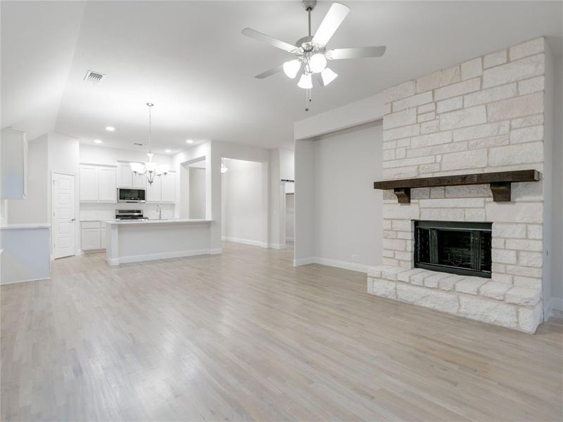 Unfurnished living room featuring ceiling fan with notable chandelier, light wood-type flooring, a fireplace, and lofted ceiling