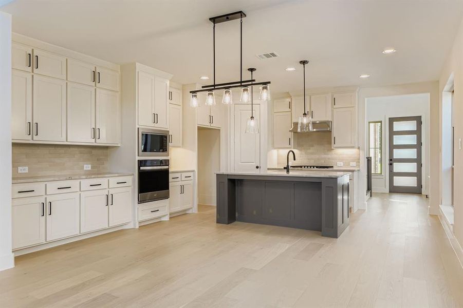 Kitchen with oven, stainless steel microwave, under cabinet range hood, decorative backsplash, and light wood-type flooring Kitchen with oven, stainless steel microwave, under cabinet range hood, decorative backsplash, and light wood-type flooring