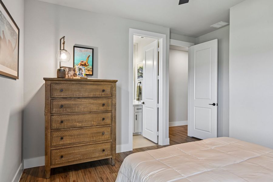 Bedroom with wood dresser, hardwood floors, and open door leading to ensuite bathroom