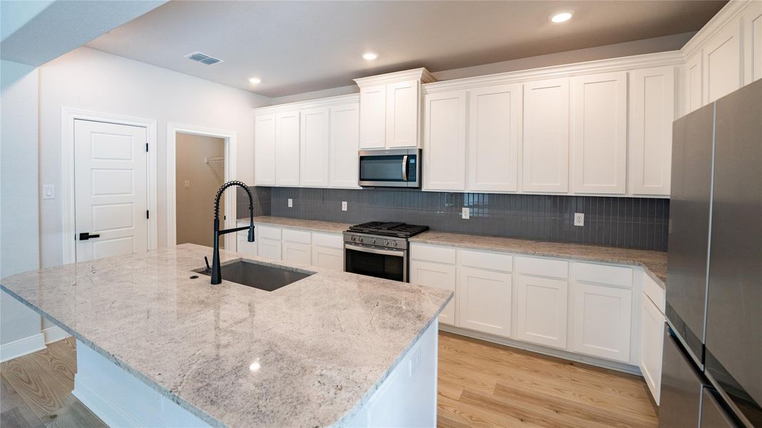 Kitchen featuring white cabinets, stainless steel appliances, light stone countertops, tasteful backsplash, and light wood-style flooring Kitchen featuring white cabinets, stainless steel appliances, light stone countertops, tasteful backsplash, and light wood-style flooring