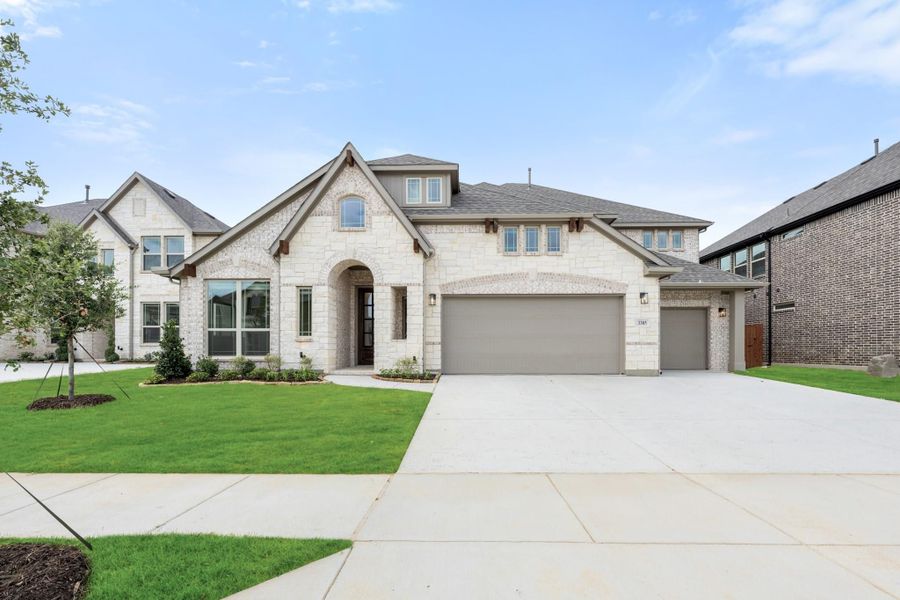 Two-story home with light stone exterior, arched entry, three-car garage, and manicured front lawn Two-story home with light stone exterior, arched entry, three-car garage, and manicured front lawn