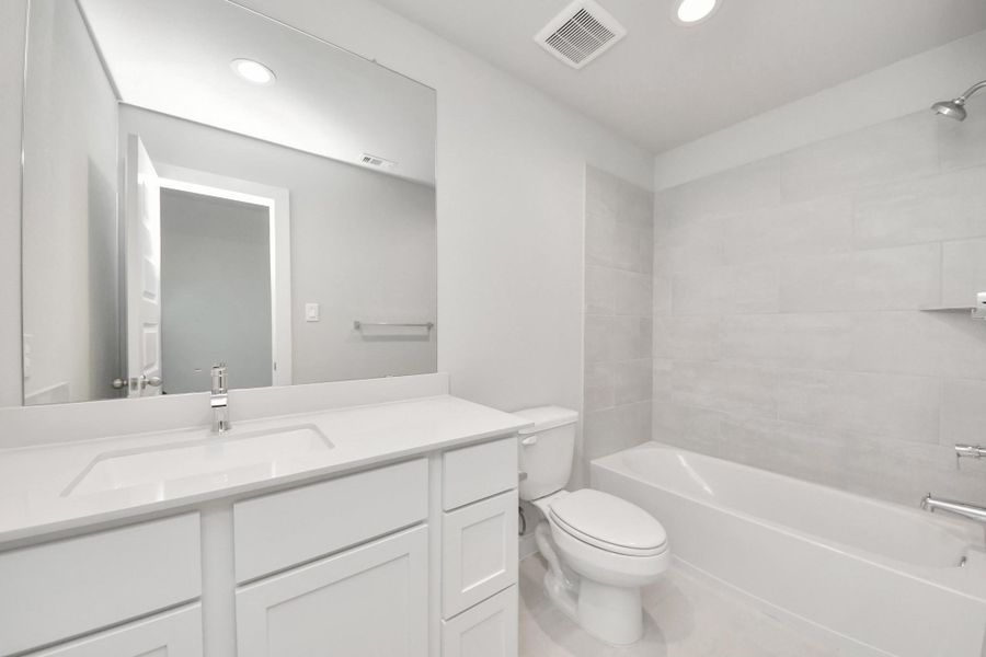 Secondary bath features tile flooring, bath/shower combo with tile surround, light stained wood cabinets, beautiful light countertop.