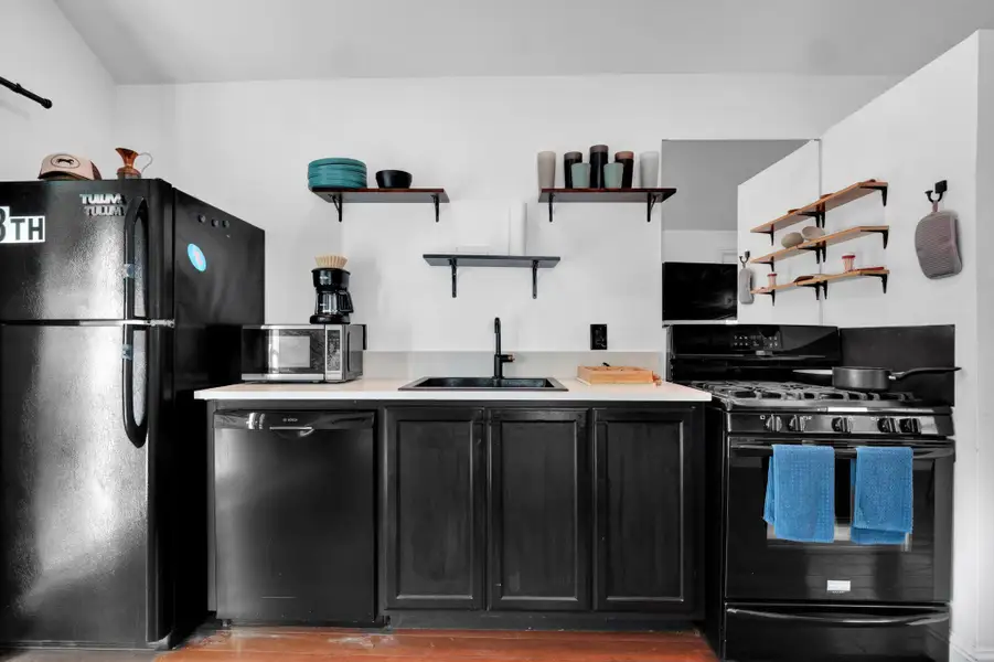 Kitchen with black appliances, open shelves, dark cabinetry, wood finished floors, and light countertops