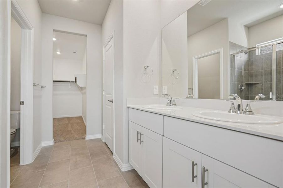 Full bath featuring a walk in closet, double vanity, a stall shower, and light tile patterned floors