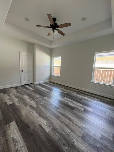 Spare room with baseboards, a raised ceiling, dark wood-style flooring, and a ceiling fan