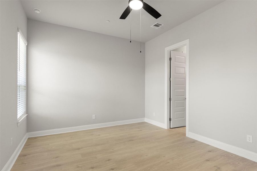Empty room featuring light wood-style flooring, a ceiling fan, and healthy amount of natural light
