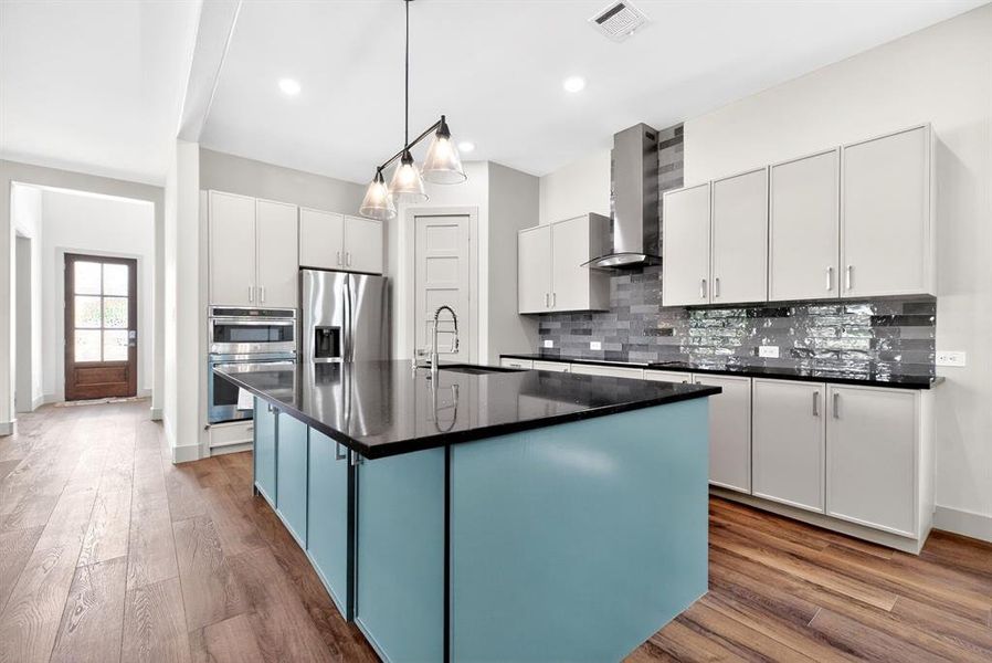 Kitchen featuring an island with sink, stainless steel appliances, dark wood-type flooring, tasteful backsplash, and pendant lighting Kitchen featuring an island with sink, stainless steel appliances, dark wood-type flooring, tasteful backsplash, and pendant lighting