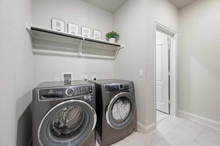 Spacious laundry area includes storage shelf with hanging rack and tiled floors