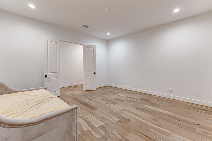 This is a spacious, empty room with light wood flooring and white walls, featuring recessed lighting and double doors. Its neutral design offers a blank canvas for customization. The following three renderings depict a few possible uses for this room.