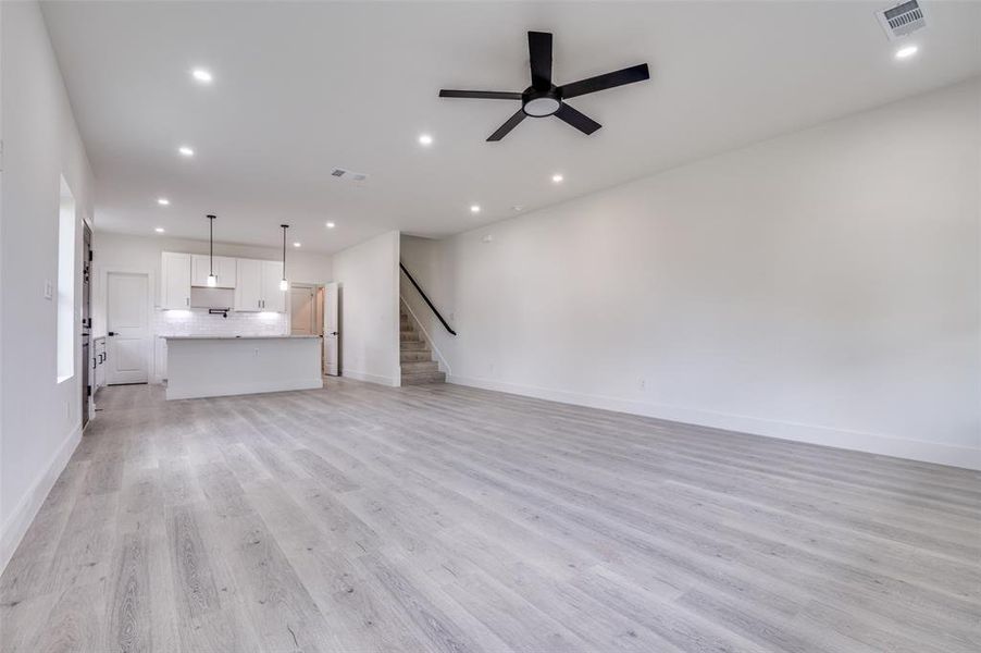 Unfurnished living room featuring light wood-style floors, ceiling fan, recessed lighting, and stairway Unfurnished living room featuring light wood-style floors, ceiling fan, recessed lighting, and stairway