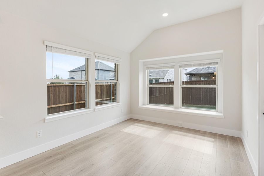 Empty bedroom with vaulted ceiling, light wood floors, and four large windows with backyard views
