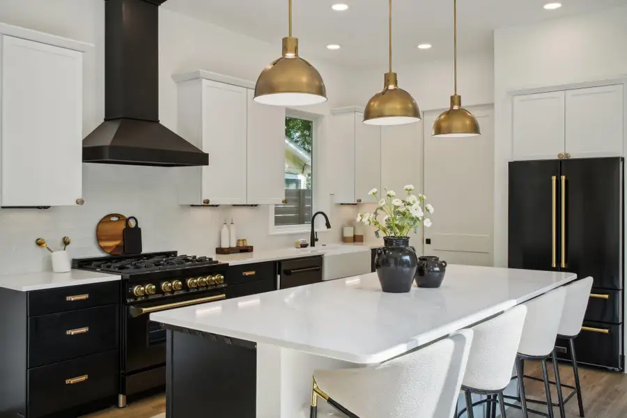 Kitchen featuring high end appliances, white cabinets, wall chimney range hood, dark cabinetry, and pendant lighting