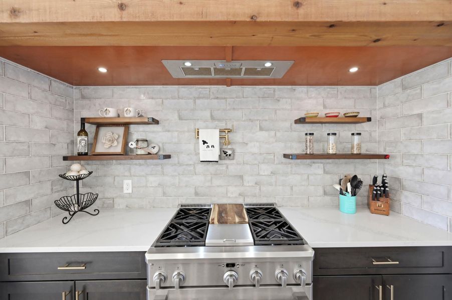 Modern culinary station features a professional gas range set against a full-height tile backsplash.