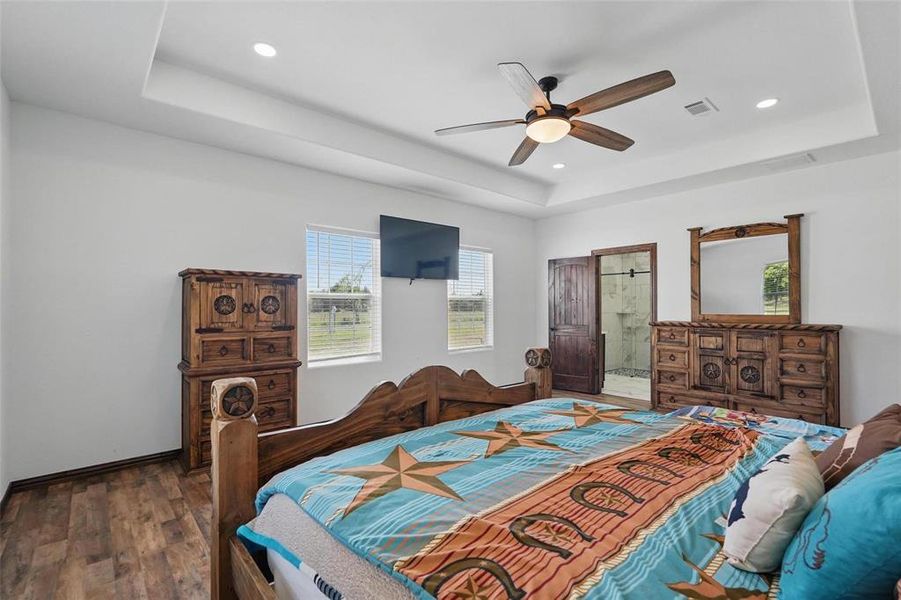 Bedroom with a tray ceiling, wood finished floors, ceiling fan, ensuite bathroom, and recessed lighting Bedroom with a tray ceiling, wood finished floors, ceiling fan, ensuite bathroom, and recessed lighting