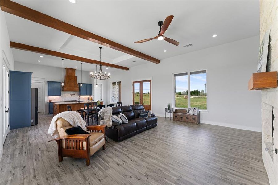 Spacious open-concept living area featuring wood-finish flooring, vaulted ceilings with exposed wood beams, and recessed lighting