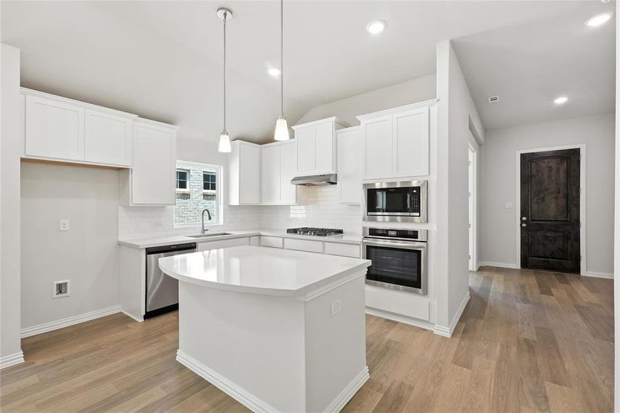Kitchen with appliances with stainless steel finishes, under cabinet range hood, backsplash, light wood finished floors, and a kitchen island Kitchen with appliances with stainless steel finishes, under cabinet range hood, backsplash, light wood finished floors, and a kitchen island