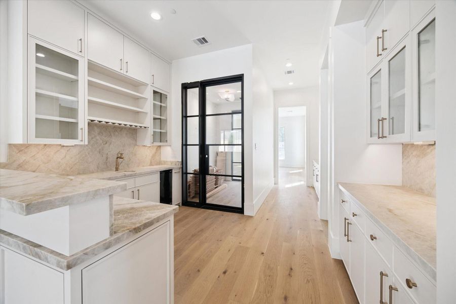 This photo showcases a sleek extension of the kitchen with white cabinetry, glass-front cabinets, and additional entertaining space. Just steps to your climate-controlled wine room. This photo showcases a sleek extension of the kitchen with white cabinetry, glass-front cabinets, and additional entertaining space. Just steps to your climate-controlled wine room.