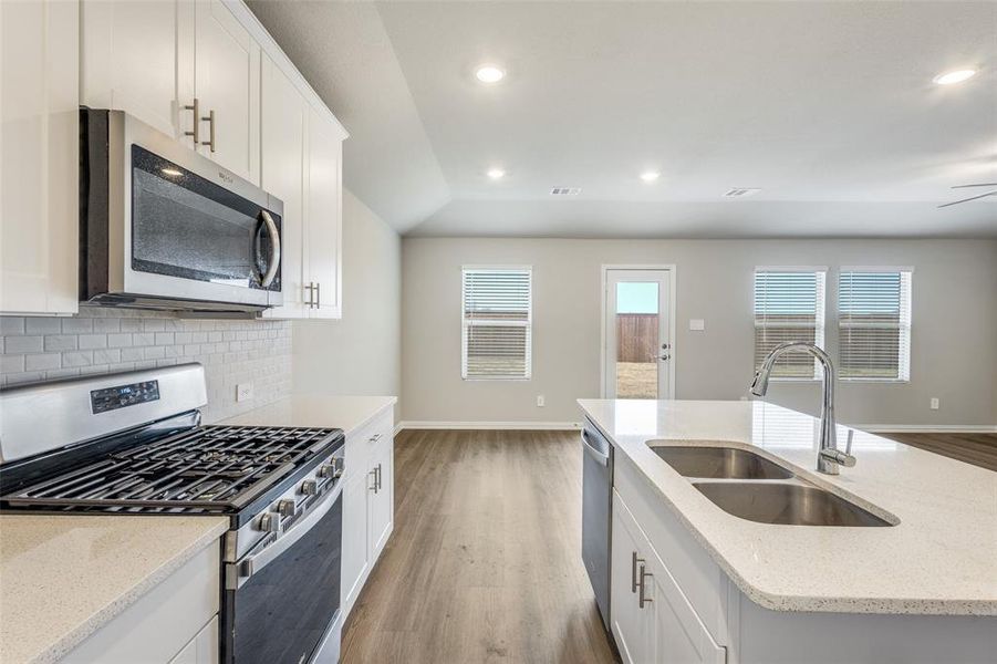 Kitchen with appliances with stainless steel finishes, white cabinetry, light stone counters, tasteful backsplash, and dark wood finished floors