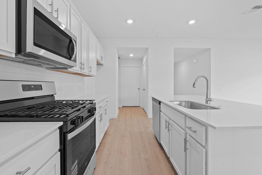 Kitchen featuring appliances with stainless steel finishes, white cabinets, light wood-style floors, recessed lighting, and light stone counters