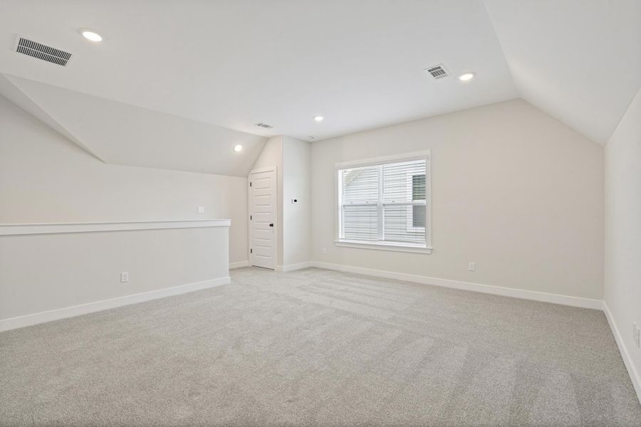 Loft space featuring soft gray carpeting, a single window with blinds, recessed lighting, a built-in railing, and a paneled door Loft space featuring soft gray carpeting, a single window with blinds, recessed lighting, a built-in railing, and a paneled door