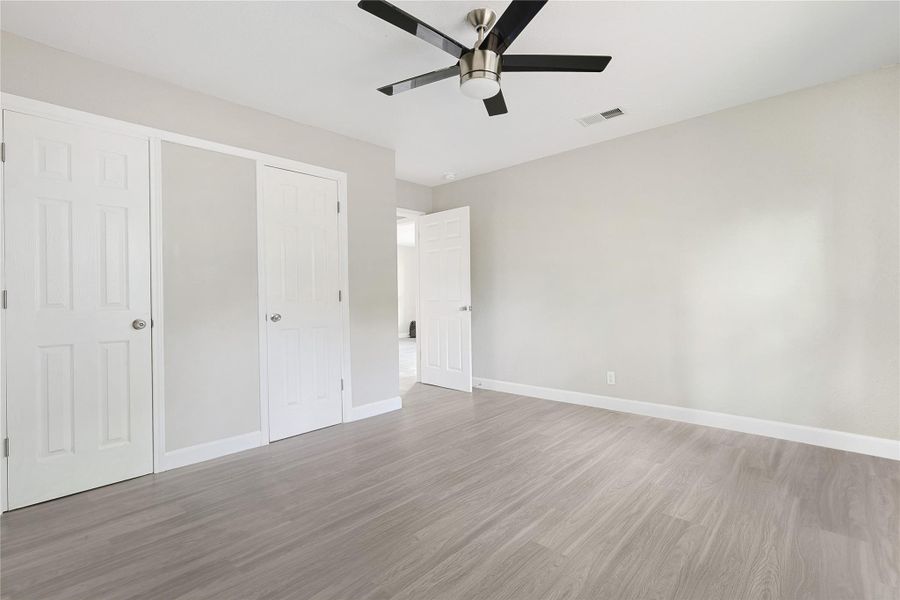 This room features neutral-toned walls and light wood flooring, creating a bright and modern atmosphere. It includes double closet doors and a ceiling fan, offering both storage and comfort.