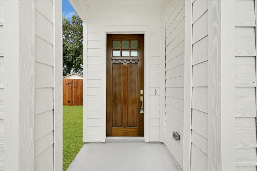 Charming front entry with a wooden door featuring decorative glass panes. The porch is framed by white siding, offering a clean and inviting look. A glimpse of a fenced yard with greenery can be seen, adding to the home's appeal. Charming front entry with a wooden door featuring decorative glass panes. The porch is framed by white siding, offering a clean and inviting look. A glimpse of a fenced yard with greenery can be seen, adding to the home's appeal.