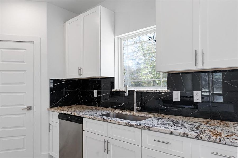 Kitchen featuring decorative backsplash, light stone counters, sink, dishwasher, and white cabinetry