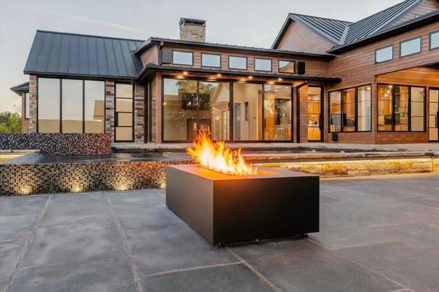 Courtyard-style outdoor living space with a contemporary fire feature, covered patio, and softly lit architectural details creating a warm nighttime atmosphere.