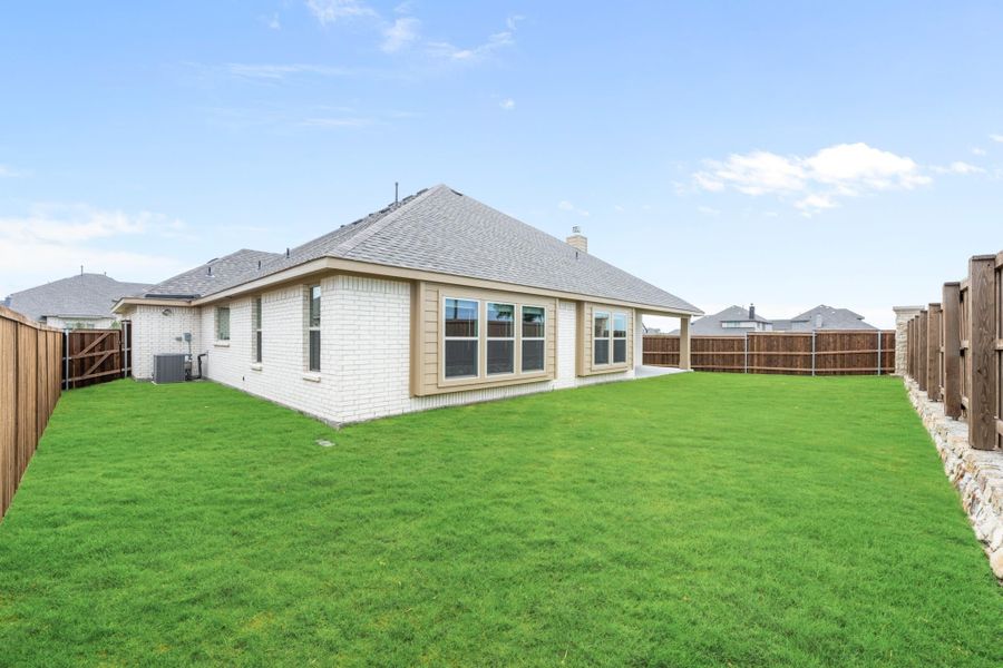 Back of single-story brick home with large fenced backyard and green lawn