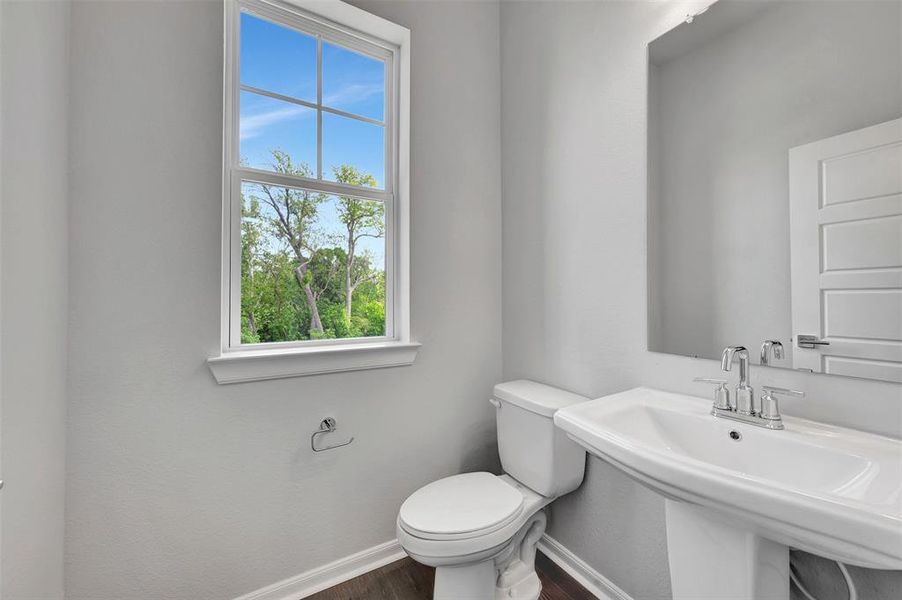 Pedestal sink with chrome hardware, framed mirror, and a single window offering natural light
