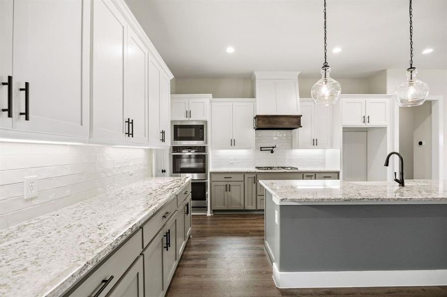 Kitchen featuring light stone countertops, hanging light fixtures, dark wood-type flooring, tasteful backsplash, and stainless steel appliances Kitchen featuring light stone countertops, hanging light fixtures, dark wood-type flooring, tasteful backsplash, and stainless steel appliances
