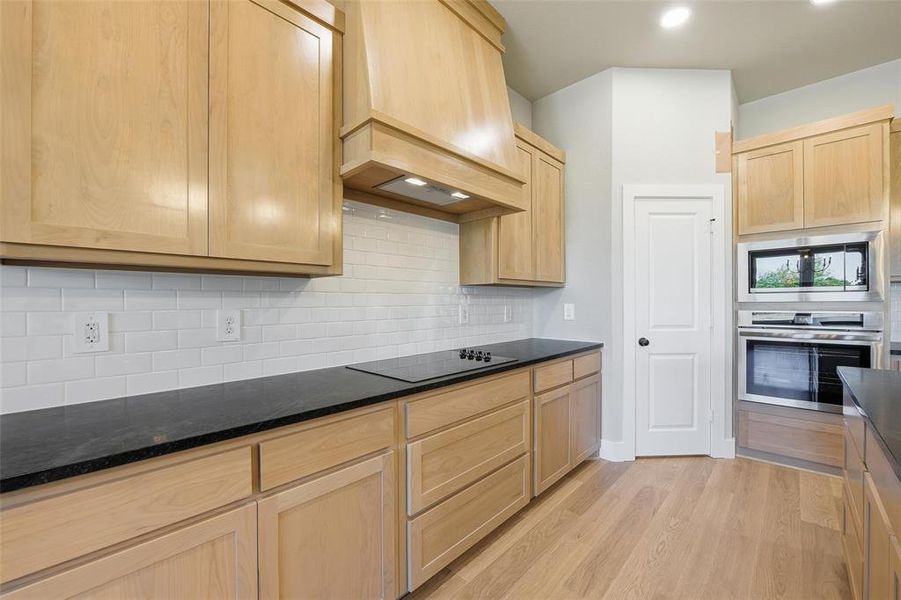 Kitchen featuring light brown cabinets, oven, light wood-style floors, decorative backsplash, and custom exhaust hood