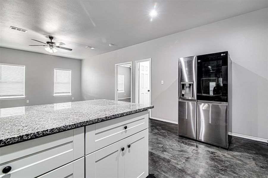 Kitchen featuring ceiling fan, white cabinets, light stone countertops, stainless steel fridge with ice dispenser, and dark tile patterned floors