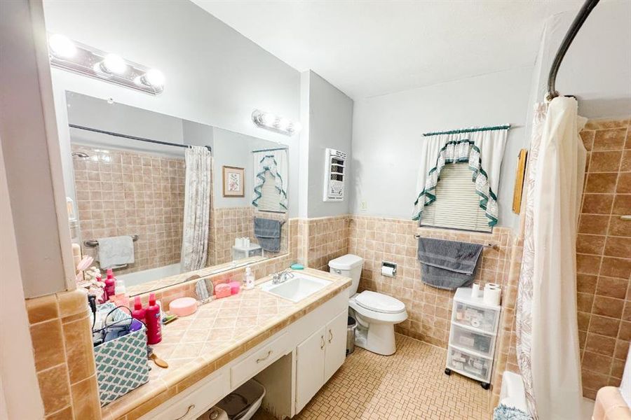 Full bathroom featuring light tile patterned floors, tile walls, vanity, shower / bathtub combination with curtain, and a wainscoted wall