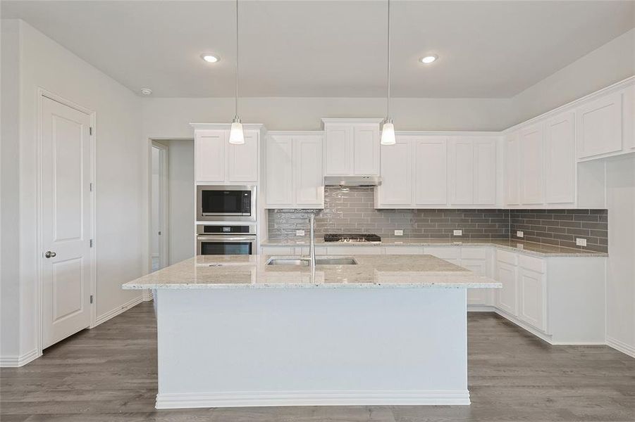 Kitchen with appliances with stainless steel finishes, white cabinets, and a center island with sink