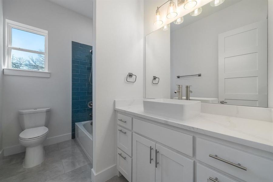 Full bathroom with tiled shower / bath combo, vanity, tile patterned floors, and toilet