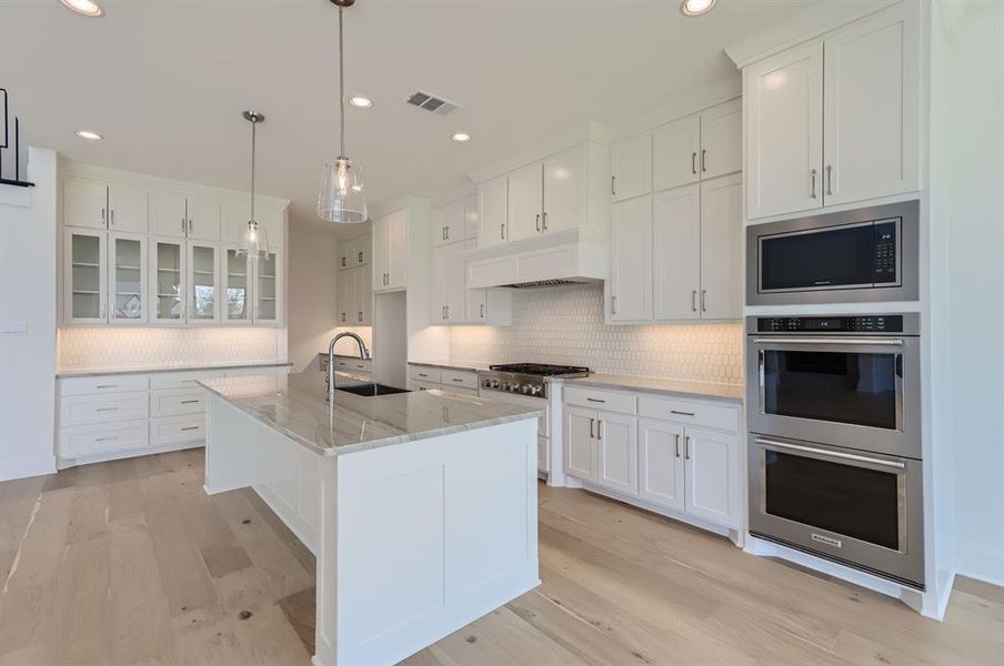 Kitchen featuring an island with sink, white cabinetry, custom range hood, and sink