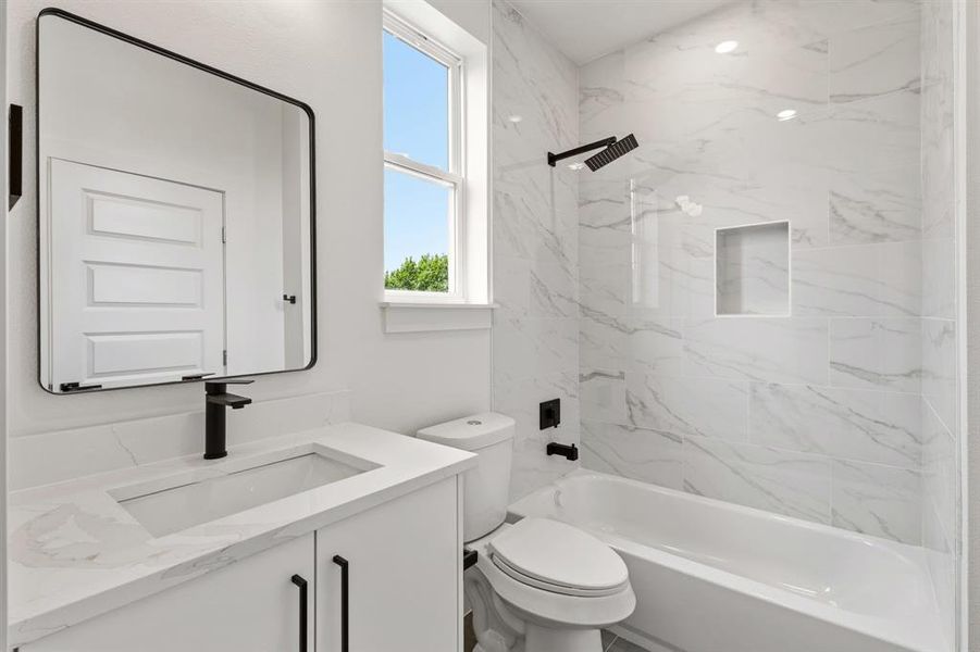 The bathroom features a vanity with a white countertop and black fixtures, a contemporary mirror, and a bathtub with white and gray tiled walls