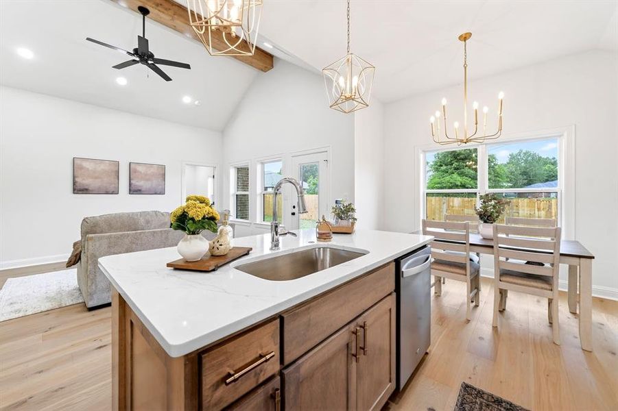 Open-concept living space featuring a vaulted ceiling with exposed beam, wood-finish flooring, a kitchen island with stone countertop and undermount sink, and recessed lighting throughout