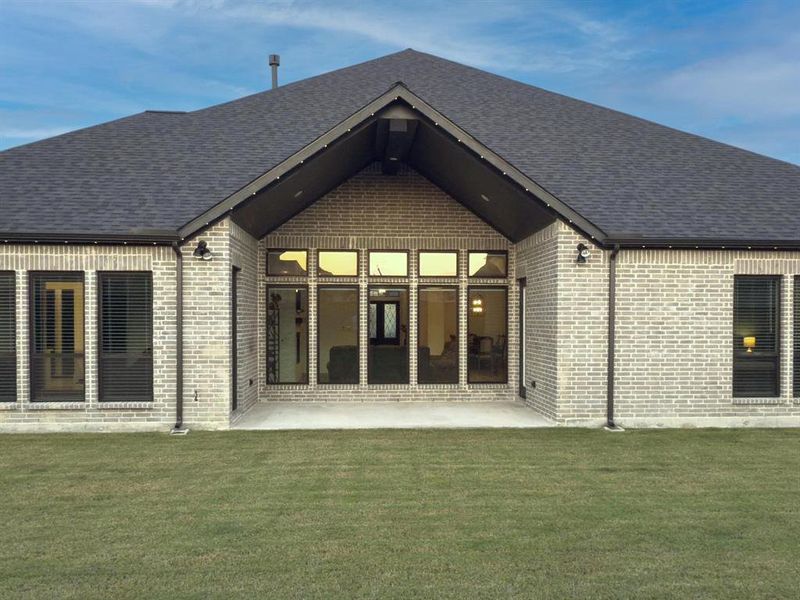 Rear view of house featuring a patio, brick siding, a lawn, and roof with shingles Rear view of house featuring a patio, brick siding, a lawn, and roof with shingles