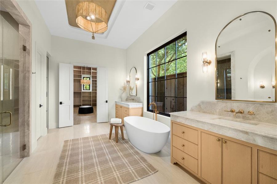 Spacious bathroom featuring a freestanding soaking tub, dual vanity with stone countertops, a large walk-in shower with glass enclosure, a prominent window with grid detailing, and a vaulted ceiling with a decorative light fixture