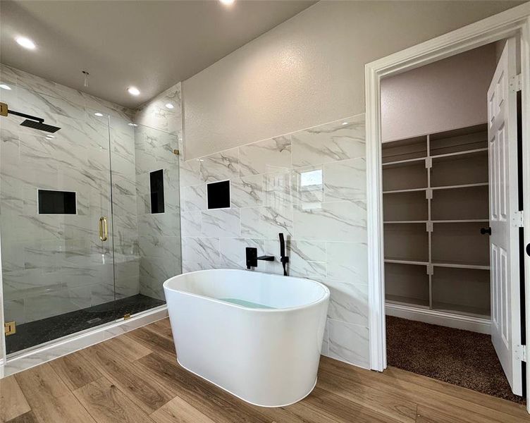 Full bathroom featuring tile walls, a marble finish shower, a soaking tub, a spacious closet, and wood finished floors