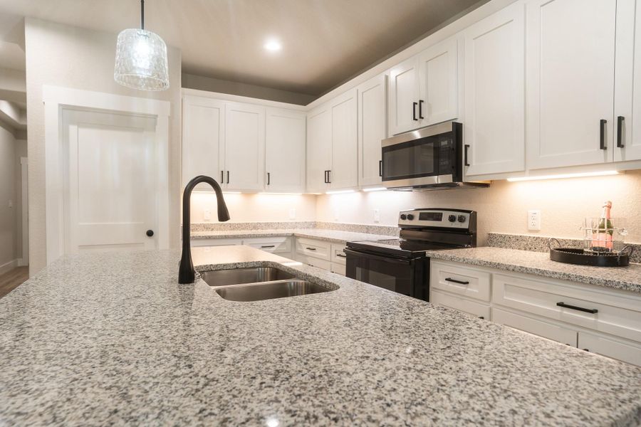 Kitchen with electric range oven, stainless steel microwave, a sink, and white cabinets