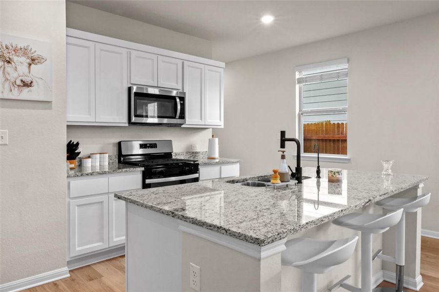 Kitchen with stainless steel appliances, white cabinetry, light wood-style flooring, light stone counters, and recessed lighting