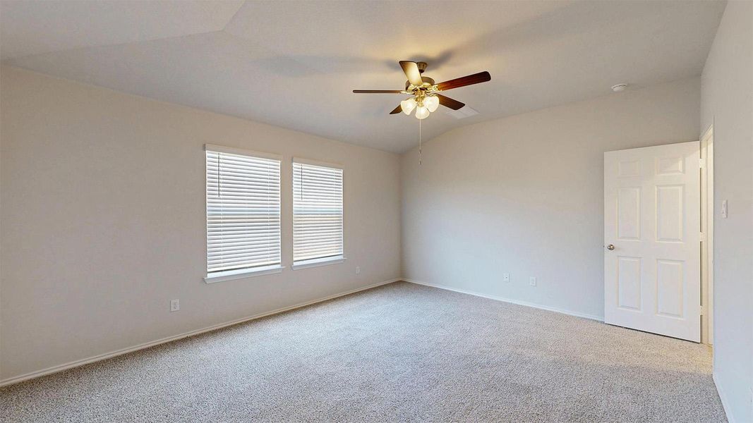 Well-lit room featuring vaulted ceilings, plush carpeting, and a versatile ceiling fan.