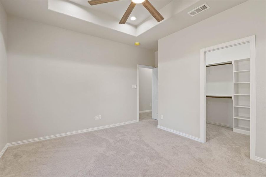 Unfurnished bedroom with a raised ceiling, ceiling fan, light colored carpet, and a closet