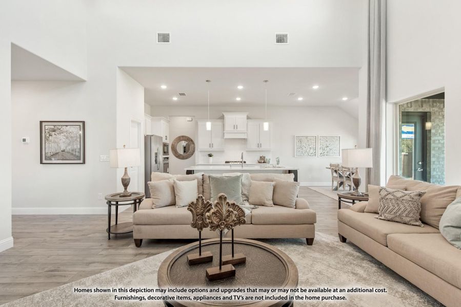 Open-concept living room with high ceilings and hardwood floors, open to white kitchen with island in background.