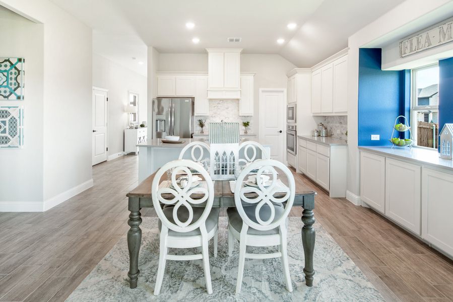 Open dining area with wood table and white chairs, connected to kitchen with white cabinets and hardwood floors