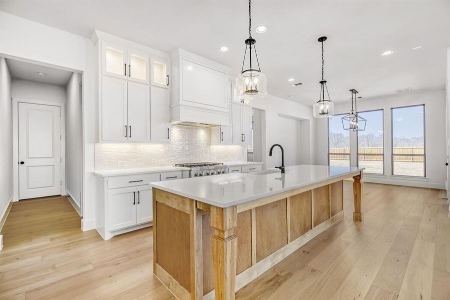 Dual tone kitchen with a kitchen island with sink, light wood-style flooring, backsplash, glass insert cabinets, and two tone cabinetry